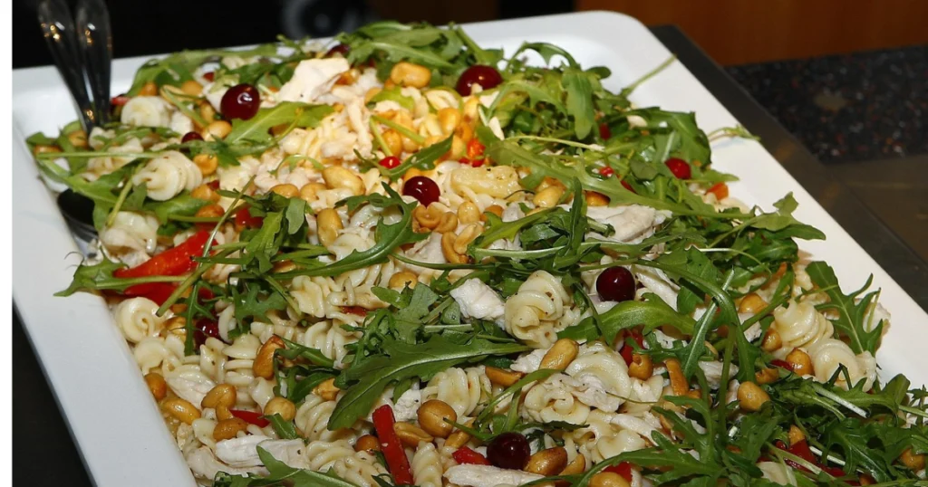 A bowl of cowboy pasta salad with crispy bacon, cherry tomatoes, black beans, cheese, and a creamy dressing, garnished with fresh herbs.